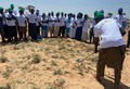 This image shows a person in the foreground with a shovel being watched by a group of people in the background